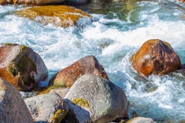 Akan suyun güzelliğini ve doğanın huzurlu manzaralarını yakalayın. Doğadaki ahenk ve sükunete odaklan. Dağınık taşların estetik çekiciliğini vurgula
