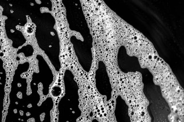 Sabun köpükleri yüzeyde kabarcıklı bir doku oluşturur. Deterjan, bulaşık yağının erimesine ve kirlenmesine yardımcı olur. Siyah tabaka zıtlaşıyor ve sabun köpüklerini vurguluyor..