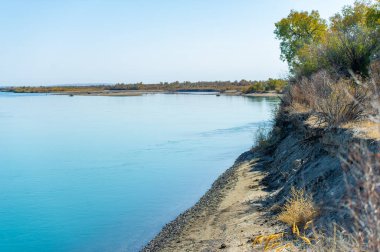 Bozkırdaki nehir. Çayırlar. Çölün kurak kalbini kesen dingin bir vaha, bu büyüleyici nehir etrafındaki bozkırlara canlı sonbahar renklerinin çarpıcı bir yansımasını saçar.