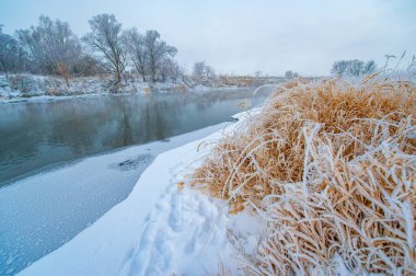 Donmuş nehir güneşin sıcak altın ışığını yansıtır. Doğal güzellikle sakin bir kış harikalar diyarı sahnesi yarat. Ufukta yükselen güneşin sükunetini yakala..