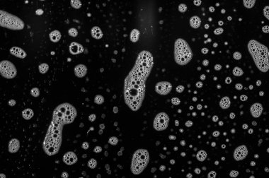 Sabun köpükleri yüzeyde kabarcıklı bir doku oluşturur. Deterjan tabakta parlak bir kalıntı bırakıyor. Siyah plaka, beyaz sabun köpüğü ve deterjan arasında bir kontrast oluşturuyor..