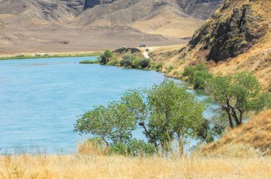 Sakin bir nehrin üzerinde günbatımının dinginliği. Görkemli dağların ve yemyeşil ağaçların nefes kesici manzarasının tadını çıkar. Doğanın güzelliğini hisset ve bu çarpıcı yerde huzuru bul..