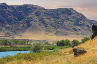 Huzurlu nehrin üzerinde günbatımının huzurlu sükuneti. Görkemli dağların ve yemyeşil ağaçların güzelliğine dalın. Rahatlamak, meditasyon yapmak ya da doğanın güzelliğinden zevk almak için ideal bir yer.