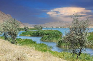 Huzurlu ve nefes kesici doğa manzarasının tadını çıkar. Nehrin üzerinde gün batımını izle. Resimli bir sahne yaratıyor. Dağların ve akan nehrin etrafındaki ağaçların huzurunun tadını çıkar..