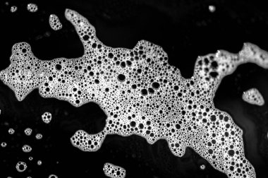 Sabun köpükleri yüzeyde kabarcıklı bir doku oluşturur. Deterjan tabakta parlak bir kalıntı bırakıyor. Siyah plaka, beyaz sabun köpüğü ve deterjan arasında bir kontrast oluşturuyor..