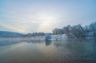 Donmuş nehir, yükselen güneşin sıcak altın ışığıyla yıkanır. Huzurlu ve sakin bir kış harikalar diyarı. Doğal güzellik etrafını sarar..