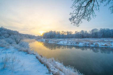 Gün doğumunda bir kış harikalar diyarının güzelliğini tecrübe et. Donmuş nehir büyüleyici bir buz manzarasına dönüşüyor. Altın güneş sihirli bir ışıkla buzlu araziyi aydınlatır..