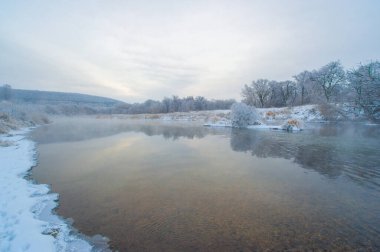 Donmuş nehir güneşin altın ışığını yansıtır. Huzur ve güzelliklerle dolu bir kış harikalar diyarı. Resimli bir ortamda sükuneti tecrübe et.