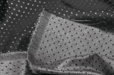 Küçük polka şeklinde metalik bir parıltıya sahip kumaş, siyah, soyut bir polikrom desen, uzay çağı estetiğine sahip siyah bir arkaplan karşısında parıldıyor ve bu kumaşa fütüristik bir gelecek hissi veriyor.