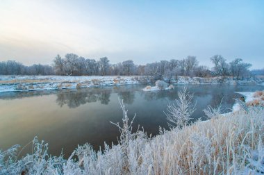 Huzurlu bir sahnede yakalanan kış harikalar diyarının güzelliği. Donmuş nehri aydınlatan altın güneş ışığı. Huzur ve doğal güzelliğin resmedilmeye değer bir gösterisi..