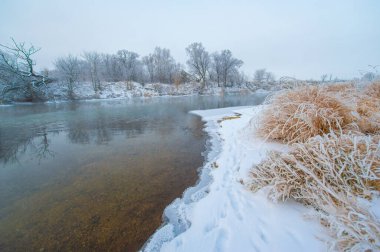 Huzurlu bir sahnede yakalanan kış harikalar diyarının güzelliği. Donmuş nehri aydınlatan altın güneş ışığı. Huzur ve doğal güzelliğin resmedilmeye değer bir gösterisi..