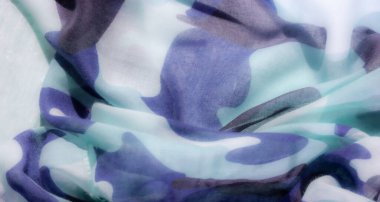Açık mavi, turkuaz ve lacivert tonlarında soyut kamuflaj desenleri olan yumuşak, akışkan kumaş, şeffaf ve desenli bir görünüm verir..