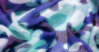 Mavi, turkuaz ve koyu gri tonlarını içeren kamuflaj desenli bir kumaş. Doku yumuşak ve şeffaf görünüyor, muhtemelen şifon gibi hafif bir malzeme..