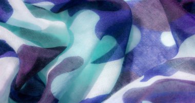 Görüntü, mavi, yeşil ve gri tonlarında soyut desenleri olan, yarı şeffaf, akıcı bir kumaşın yakın çekimini gösteriyor..