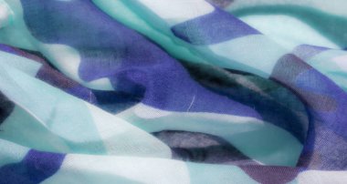 Soyut kamuflaj kumaşı, mavi, turkuaz ve koyu gri tonlarını içeren bir kamuflaj desenine sahip kumaşın yakın çekimini gösteriyor. Doku yumuşak ve şeffaf görünüyor.