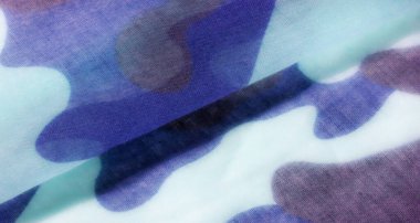 Soyut kamuflaj kumaşı, mavi, turkuaz ve koyu gri tonlarını içeren bir kamuflaj desenine sahip kumaşın yakın çekimini gösteriyor. Doku yumuşak ve şeffaf görünüyor.