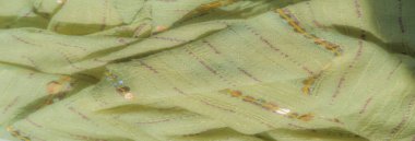 İnce pembe dikişli bulanık sarı-yeşil kumaş ve parlak pullu süslemeler. Kumaş nazikçe katlanır, yumuşak bir doku ve narin ışık yansımaları yaratır..