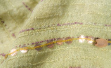 Pembe ve mor dikişli sarı-yeşil kumaşın bulanık görüntüsü. Kumaş yumuşak bir şekilde buruşmuş, parlak pullarla güçlendirilmiş, dokulu bir görünüm yaratıyor..