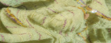 Pembe ve mor dikişli sarı-yeşil kumaşın bulanık görüntüsü. Kumaş yumuşak bir şekilde buruşmuş, parlak pullarla güçlendirilmiş, dokulu bir görünüm yaratıyor..