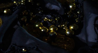Parlayan altın paraların bulanıklığı ve siyah kumaş üzerinde boncuklar, göz alıcı bir doku yaratıyor. Altın elementler ve siyah kumaş arasındaki zıtlık yüksek moda ve zarafet hissi yayıyor..