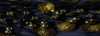 Kalıplı siyah kumaş, altın sikkeler ve boncuklarla sarmalanmış. Parlak röfle ve karmaşık işçilikle lüks ve süslü bir desen oluşturuyor..