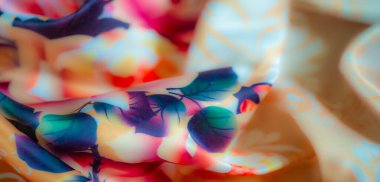 Yumuşak pembe ve şeftali tonlarında çiçek açan güllerle bezenmiş kumaşın bulanık görüntüsü yeşil yapraklar ve koyu gölgelerle karışıp sofistike bir renk yaratıyor.