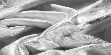 Yumuşak bir parıltıda narin bir yaprak deseni olan katlanmış beyaz bir kumaş parçası. Tasarım, materyalin doğal akışını vurgulayan lüks ve zarif bir doku yaratıyor..