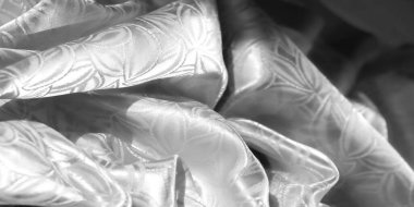 Yumuşak, yumuşak beyaz bir kumaş. Tekrarlayan çiçek motifli. Narin, ipeksi kumaşın üzerinde ışık yansıması var. Kumaş akış çizgileri ve karmaşık tasarım detayları.