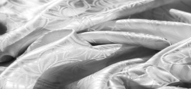 Yumuşak, yumuşak beyaz bir kumaş. Tekrarlayan çiçek motifli. Narin, ipeksi kumaşın üzerinde ışık yansıması var. Kumaş akış çizgileri ve karmaşık tasarım detayları.