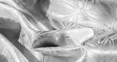 Şatafatlı, beyaz saten ya da ipek kumaş. Karmaşık, zarif bir çiçek deseni ya da bir jakoza benzer bir deseni var. Dokusunu ve parıltısını göstermek için yumuşakça örtülmüş.