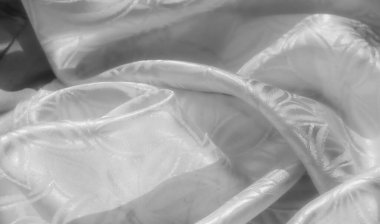 Pürüzsüz, lüks beyaz saten kumaşın yakın plan görüntüsü. Karmaşık çiçek desenleri var. Dokusunu ve detaylarını göstermek için yavaşça buruşmuş. Parlak yüzey ışığı yansıtır, narin bir parlaklık yaratır.