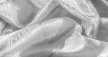 Şatafatlı, beyaz saten ya da ipek kumaş. Karmaşık, zarif bir çiçek deseni ya da bir jakoza benzer bir deseni var. Dokusunu ve parıltısını göstermek için yumuşakça örtülmüş.