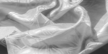 Karmaşık kabartmalı desenli beyaz saten kumaş, pürüzsüz doku ve yumuşak kıvrımlar sergiliyor. Kumaş ışığı yansıtıyor, zarif çiçek ve yaprak tasarımlarını ince bir şekilde vurguluyor.