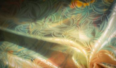 Işıldayan, çiçek desenli, altın, turuncu ve yeşil renkli kumaşların yakın çekimi. Karmaşık tasarım zarif kıvrımları ve dokuları vurguluyor. Yumuşak, aydınlık bir bitiş ile..