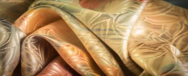 Pastel pembeler, yeşiller ve altın karışımı lüks ipek tekstil. Karmaşık bir çiçek deseni ve yumuşak ışığı yansıtıyor. Canlı ama sofistike bir estetik serpiştiriyor..