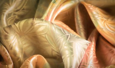 Yanardöner bir parıltı ile ipek kumaş ve yumuşak yeşil bir karışım ve şeftali tonları, karmaşık çiçek tasarımları ile vurgulanmış, lüks, akıcı bir estetik sunar.