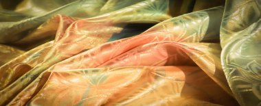 Çiçek motifli canlı kumaş, sıcak şeftali tonlarından serin yeşil ve maviye dönüşüyor, maddenin yansıtıcı parıltısı ve pürüzsüz kıvrımlarıyla vurgulanıyor..