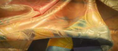 Turuncu, şeftali ve yeşil tonlarda çiçek desenli renkli saten kumaş yumuşak, ışıltılı bir dokuyu ve yüzey boyunca ışık oyunlarını göstermek için özenle katlanmış..