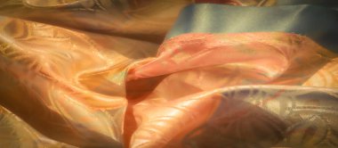 Şeftali ve altın çiçekli kumaşın üzerinde yumuşak, metalik bir parıltı. İnce yeşil aksanlı, dokusunu ve karmaşık tasarımını aydınlatan doğal ışıkla aydınlatılmış..