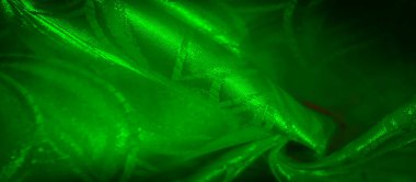 Soyut desenleri olan zengin yeşil saten kumaşa yakın plan, yumuşak ışıkta kumaşın dokusunu ve parıltısını yakalıyor..