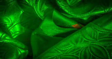 Canlı yeşil, parlak bir kumaş. Karmaşık bir yaprak gibi, akan bir desen. Kumaş ışığı yansıtır, ipeksi, pürüzsüz ve lüks bir doku yaratır. Materyaldeki kıvrımlar boyutu arttırır.