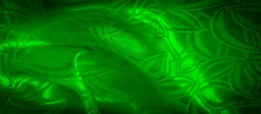 Bitkisel yaprak desenli yeşil kumaş, ışıkla hafifçe aydınlatılmış, karmaşık dokuyu ve kıvrımları vurguluyor.