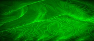 Parlak yeşil bir kumaş. Karmaşık yaprak desenleri var. Işıkla aydınlatılıyor..