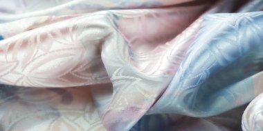 Yumuşak çiçek motifleriyle süslü, pastel renkli saten kumaş, yüzeydeki ışık oyunlarını arttıran kıvrımlar..