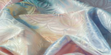 Yansıtıcı özelliklere sahip yumuşak pastel kumaş, soyut çiçek desenleri, yumuşak bir mavi saten kurdele ile örtülmüş.