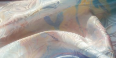 Parlak bir kaplaması olan açık ve havadar kumaş yumuşak pembe ve mavi renklerde soyut desenler sergiliyor. Kumaş biraz buruşmuş, ışık desenli yüzeyi yakalıyor..