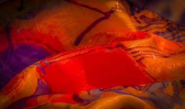 Kırmızı, turuncu ve mor renkli parlak ve soyut bir tekstil, kıvrımlı kumaş dokularını gösteriyor..