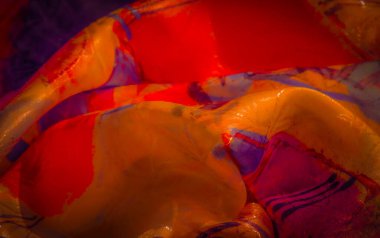 Akan dokuları ve karmaşık tasarım detaylarını gösteren soyut kırmızı, mor, sarı ve mavi karışımlı renkli bir kumaş..