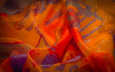 Turuncu ve mor tonlu, parlak renkli, dinamik bir kumaşın detaylı görüntüsü. Zengin doku ve akışkan desenler bunu büyüleyici kılıyor..