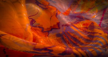 Sarı, turuncu, kırmızı ve mor renk karışımlı renkli soyut kumaş. Doku akışkan desenlerle yumuşaktır, görsel olarak dinamik ve sanatsal bir kompozisyon yaratır..